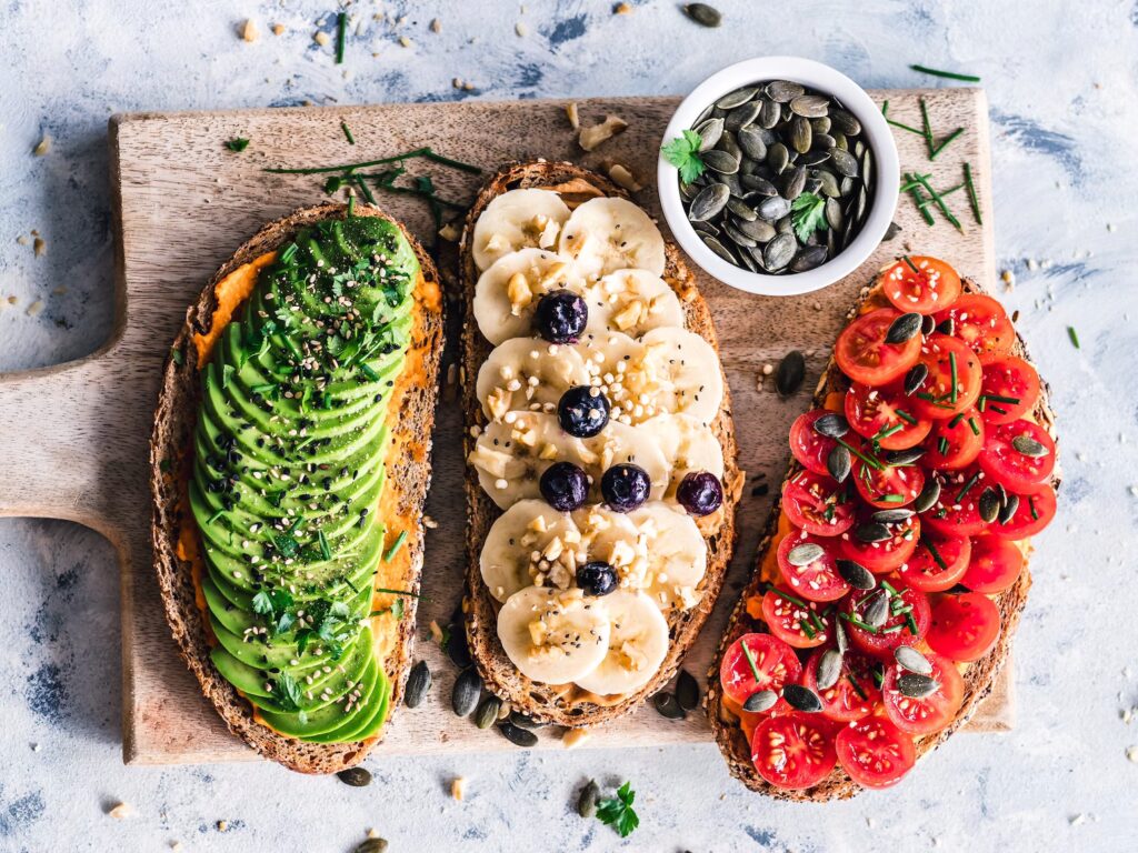 three slices of toast, each topped with different ingredients, commonly referred to as "avocado toast," "banana toast," and "tomato toast" or similar variations of open-faced sandwiches.